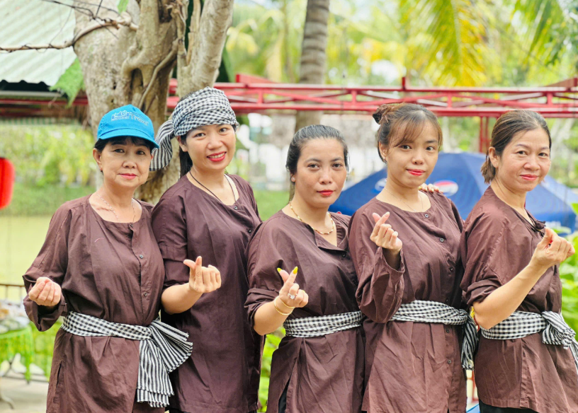 Nhóm nữ du khách mặc áo bà ba nâu truyền thống, thắt khăn rằn và tạo dáng chụp ảnh tại khu du lịch Cồn Phụng, Bến Tre.
